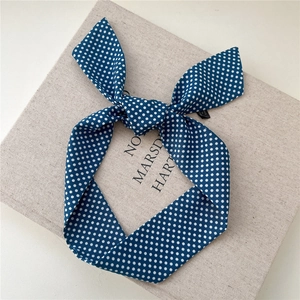 Gros plan du foulard en soie bleu à pois noué en nœud sur un livre décoratif texturé