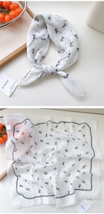 Detail showing white cotton-linen square scarf with black bow patterns and wavy edges