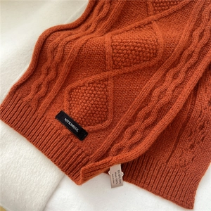 Detail view of deep orange wool scarf with thick knit patterns and 100% wool label