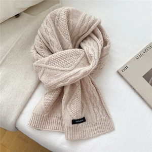 Detailed close-up of beige thick wool scarf with classic cable knit and 100% wool label