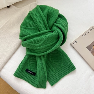 Detail of green cable knit wool scarf with 100% wool label on textured background