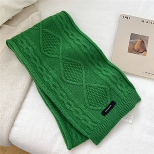 Close-up of green wool scarf showing diamond knit texture and 100% wool material label