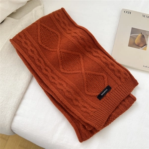 Close-up of thick terracotta cable knit wool scarf with 100% wool label on white background