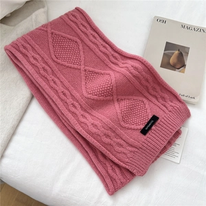 Close-up of pink wool knit scarf showing thick cable patterns and 100% wool label
