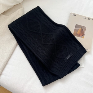 Detailed view of black cable-knit wool scarf texture with a 100 percent wool fabric label