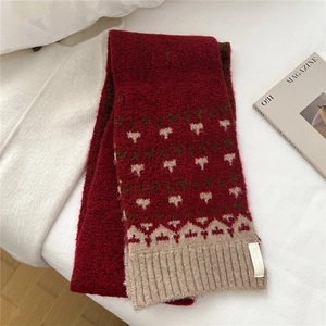 Close-up of red knit scarf with white heart pattern and ribbed edge on white fabric