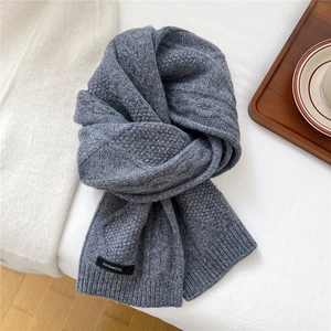 Close-up of dark grey wool scarf showing detailed cable knit texture and 100% wool label
