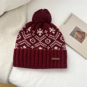 Close-up of knit winter hat featuring snowflake jacquard patterns and a large pom-pom