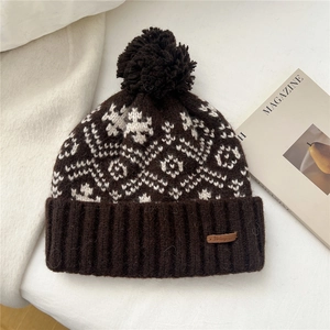 Detailed view of dark brown knitted beanie with pompom, snowflake pattern and leather patch