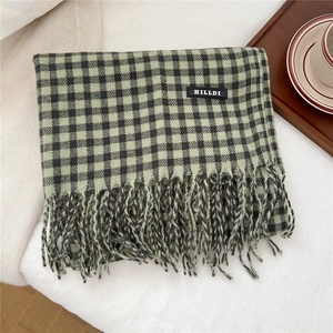 Detail eines karierten Schals mit Strickstruktur, Fransenkanten und schwarzem Markenlabel
