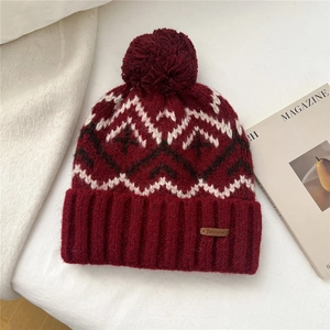 Close-up of burgundy knit hat featuring pom-pom, geometric patterns and leather label