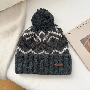 Detail of grey Fair Isle knit hat with large pom-pom and leather logo tag on white fabric