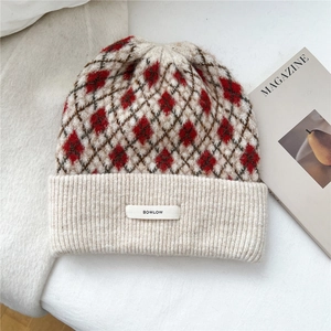 Detail of diamond pattern knit beanie with BOWLOW label on soft fabric and magazine
