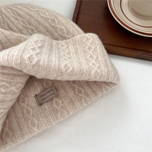Detailed view of cream-colored 100% wool cable knit hat with care label and texture