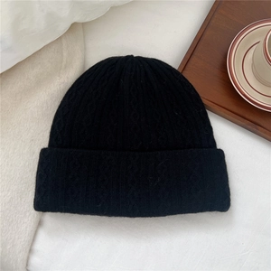 Close-up of black cable knit winter wool hat with cuffed brim on soft white fabric