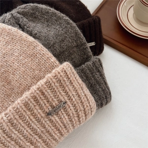 Detail of thick chunky knit beanies in pink, grey and brown with metallic logo plates