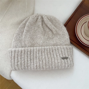 Detailed texture of oatmeal knit beanie with metallic brand tag on white surface