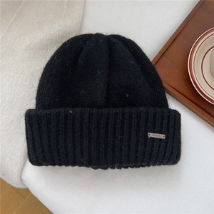 Close-up of black chunky knit beanie featuring a silver metal logo on a wooden tray