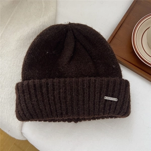 Detail of chunky knit winter beanie in dark brown with engraved metallic side logo