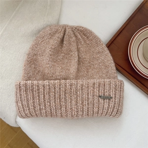 Close-up of thick knit beanie texture with a metal brand logo label on soft fabric