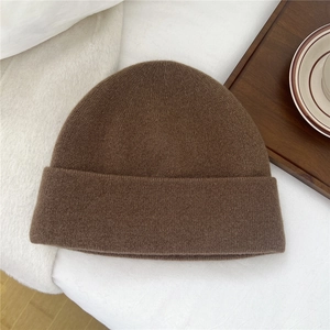 Close-up of brown wool knit beanie with fine texture on white fabric with coffee cup