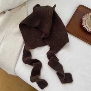 Close-up of a dark brown knitted balaclava with cute ears and scarf on white bedding