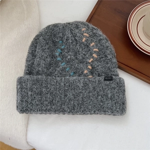 Detailansicht der grauen Strickmütze mit blauen und beigen Kontrastnähten und Logo