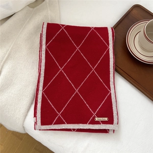 Detail of red diamond lattice knit scarf with brand logo plate on white fabric