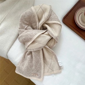 Close-up of diamond pattern knit scarf with metal brand tag and soft texture detail