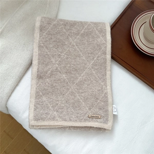 Close-up of diamond pattern knit scarf with metal logo tag and coffee cup decor