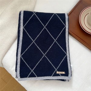Detail of navy knit scarf with grey diamond pattern and gold brand tag on white fabric