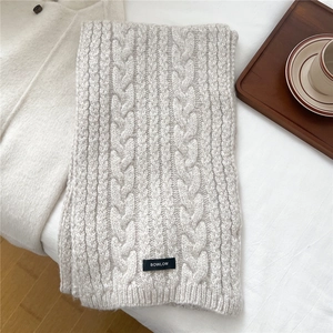 Detail of cream cable-knit wool scarf with BOWLOW label on a soft winter backdrop
