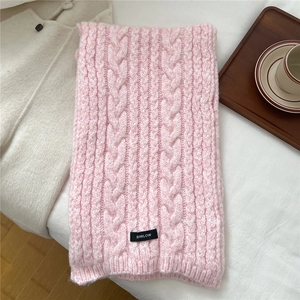 Detail of pink cable knit scarf with a woven black brand label on soft wool fabric