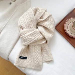 Detail of chunky knit scarf with cable pattern and woven brand label on white fabric