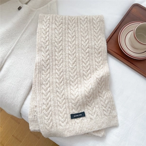 Close-up of cable-knit texture on beige wool blend scarf with a minimalist brand label