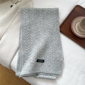 Detailed view of grey cable knit wool scarf with a brand label on soft bedding background