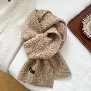 Detail of camel wool blend knit scarf featuring classic cable knit texture and woven label