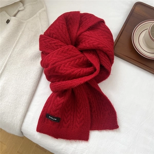 Close-up of red chunky cable knit wool scarf texture with brand woven label on white background