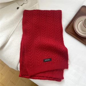 Detail of red cable-knit wool blend scarf with brand label on a warm winter background