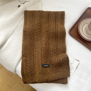 Detail of a brown chunky knit wool scarf with twist pattern and logo tag near coffee cups