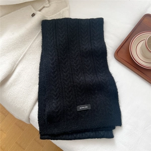 Detail of black cable-knit wool scarf with branded woven label on a cozy background