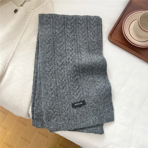 Detail of grey cable knit wool scarf with brand label on cozy minimalist background