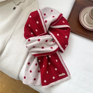 Dettaglio di sciarpa in lana a pois rosso e crema con texture in maglia morbida su letto