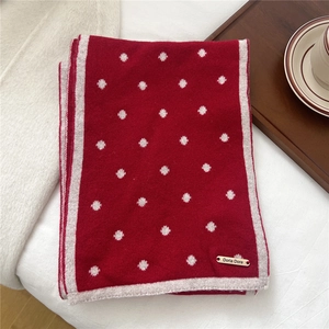 Dettaglio sciarpa di lana rossa a pois con logo metallico e bordo a costine
