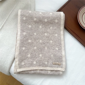 Dettaglio della sciarpa in lana a pois con placca logo su tessuto a maglia beige