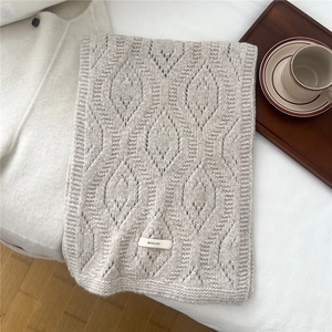 Detail of grey hollow knit wool scarf with BOWLOW brand label on a cozy white bed