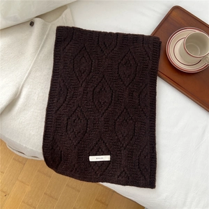 Detailed knit texture of dark brown wool blend scarf with brand label on a cozy bed