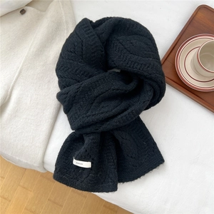 Close-up of black cable knit wool scarf with a white logo tag and soft texture
