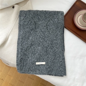 Macro detail of dark grey wool blend cable knit scarf with brand label on white bedding