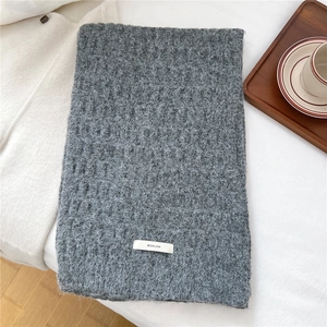 Detailed texture of thick grey wool knit scarf with BOWLOW woven label on white surface